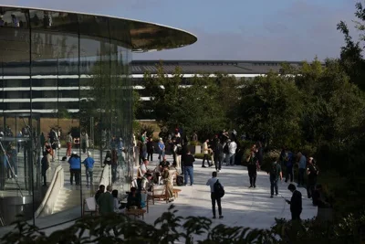 People wait inside and outside the Steve Jobs Theater, a rounded glass building.