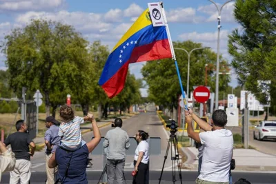 People standing outside looking at a road. One man waves a Venezuelan flag. 