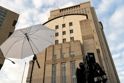 A video camera and umbrella are seen set up in front of a large building.