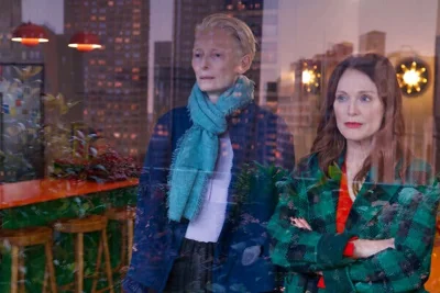 Two women look through a window with a cityscape reflected in the image.