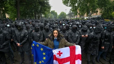 A woman holds a Georgian national and an EU flags in front of riot police blocking a street