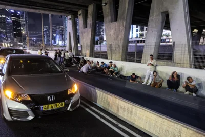 People take cover behind vehicles under a bridge in Tel Aviv