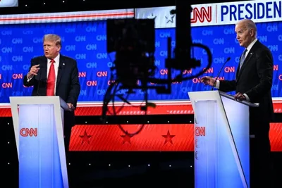Donald Trump and Joe Biden stand at lecterns on CNN’s debate stage, a TV camera in foreground