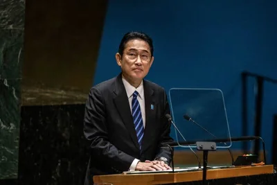 Fumio Kishida, wearing a dark suit, stands behind a lectern. 