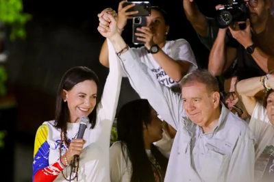 Maria Corina Machado and Edmundo Gonzalez hold hands, lifting their arms in the air at a rally.