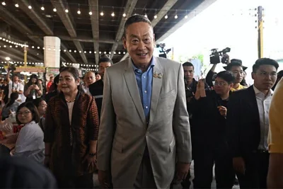 Prime Minister Srettha Thavisin of Thailand walks with dozens of people under a concrete structure. 