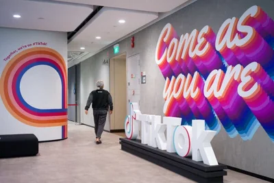 A person walks by a 3-D rendering of the TikTok logo in an office lobby, with colorful writing painted on the wall that reads, "Come as you are."