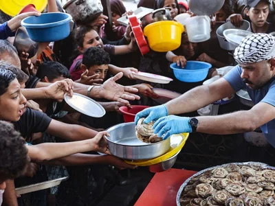 Palestinian children hold out their plates toward a man