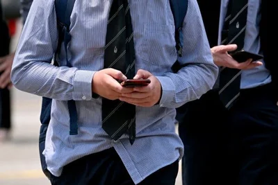 Two boys wearing school uniforms looking at their phones.