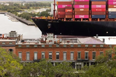 A container ship passes along buildings lining a river.