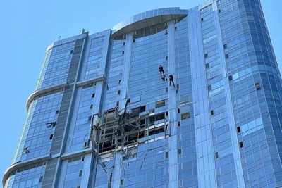 A high-rise glass building with windows blown out on several stories.