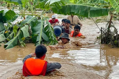 Rescuers in orange vests help people through floodwaters that have reached the tops of banana trees.