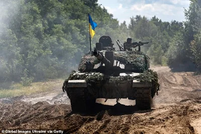 A Ukrainian soldier with a machine gun in his hands rides along a dirt road on a Challenger-2 tank on August 3, 2023