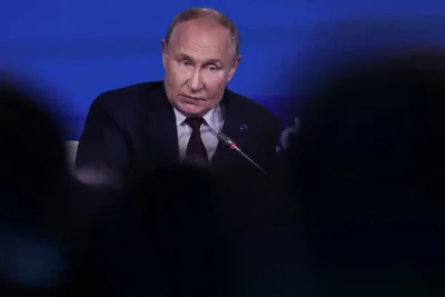 President Putin of Russia in front of a microphone and against a blue background.