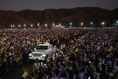 A large crowd gathers around a white truck carrying the pope.