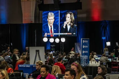 Reporters in the “spin room” at the debate, with a large screen in the background showing Donald Trump and Kamala Harris.