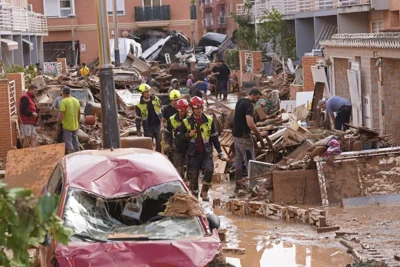 Firefighters walk as people try to clear up the damage after floods