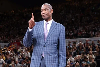 Dikembe Mutombo standing on a court wearing a suit with his index finger extended. 