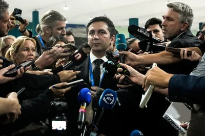 Yalchin Rafiyev, in a dark suit, surrounded by journalists holding out microphones. 