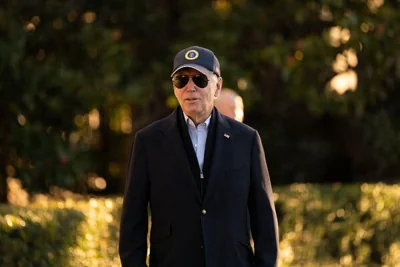 President Biden wearing a dark suit jacket, baseball cap and aviator sunglasses