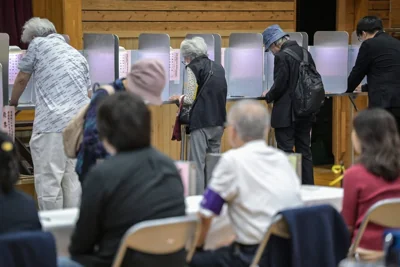 Officials look on as people vote during the general election at a polling station set up at a local school in Tokyo on October 27, 2024.  AFP PHOTO