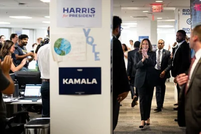 Kamala Harris claps her hands together and smiles as campaign staff applaud her arrival. She is walking through her  campaign headquarters.