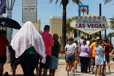 A person standing in line near a sign that reads “Welcome to Fabulous Las Vegas” is covered by a blanket to protect against the sun. 