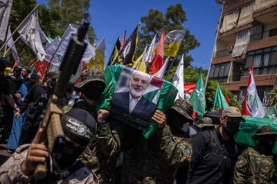 A large group parades through a street with various flags and a picture of Ismail Haniyeh.