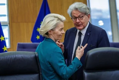 Ursula von der Leyen and a man stand close together near chairs with European Union flags behind them.