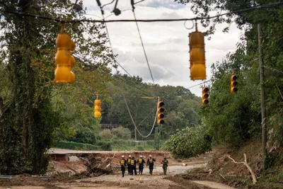 Emergency workers make their way through a washed-out area as damaged traffic lights dangle overhead.