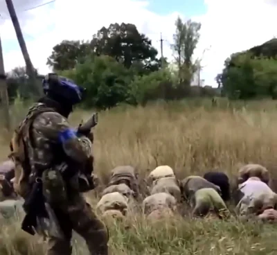 A Ukrainian soldier stands above dozens of Russian troops as they surrender on their knees