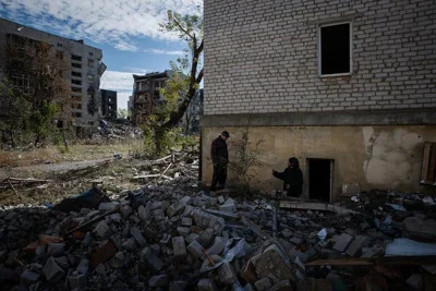 Two people among rubble outside a damaged building.