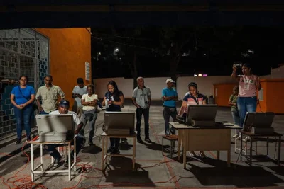 A group of people stand and sit in front of computers in a courtyard at night.