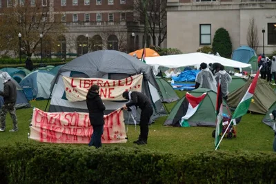Colorful tents fill a lawn at Columbia University. Pro-Palestinian, some in rain ponchos, mill about. 