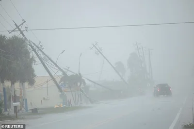 A motorist drives past broken utility poles downed by strong wind gusts as Hurricane Milton approaches Fort Myers, Florida