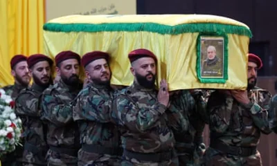 Men in camouflage military uniform and wearing red berets carry a yellow-shrouded coffin which has a picture of Nasser attached to its front