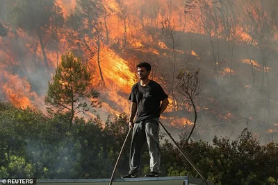 STAMATA -- A volunteer stands on a roof as flames rise from a wildfire burning behind