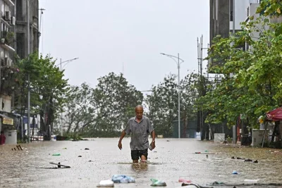 A man walking in knee-deep water in what appears to be a flooded road.