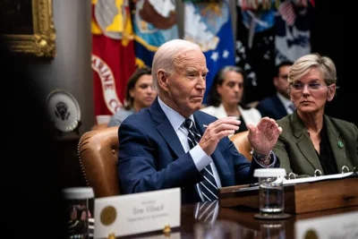 President Biden sitting at a table and gesturing with his hands.