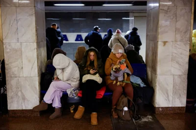 Three women huddle up in winter clothes in an underground Kyiv metro station