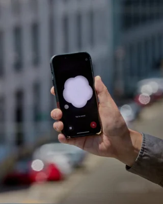 A hand holding up a phone. The screen of the phone has a white cloudlike object set against a black background.
