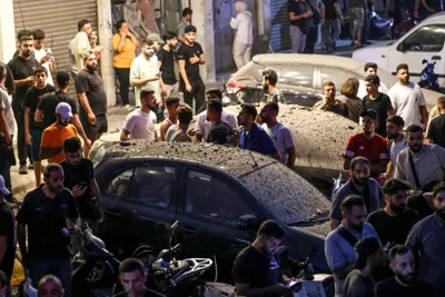 Image: LBystanders surrounded vehicles covered in debris near the site of an Israeli military strike on Beirut's southern suburbs 