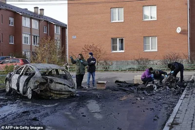 Russian law enforcement officers inspect the wreckage of a drone next to a burnt-out car in the courtyard of residential buildings following a drone attack in the village of Sofyino, Moscow region, on November 10