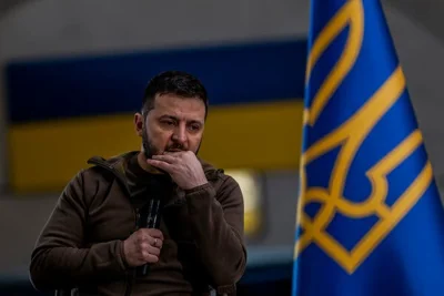 A man holds a microphone as he behind a blue flag.