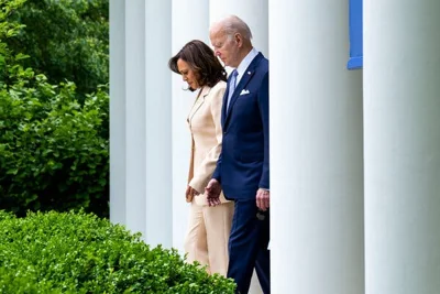 Vice President Kamala Harris and President Biden stepping into the Rose Garden. She is wearing a cream pantsuit and he is wearing a blue suit.