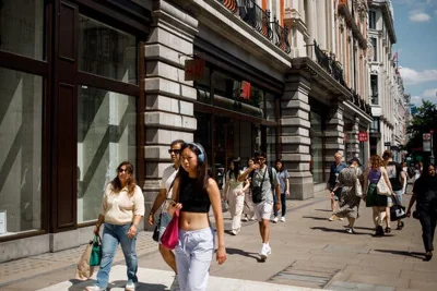 People walking down a sunny London street, with shopping bags and stores behind them. 