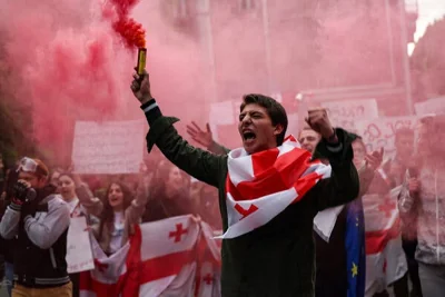 A man draped in a flag holds a red flare.