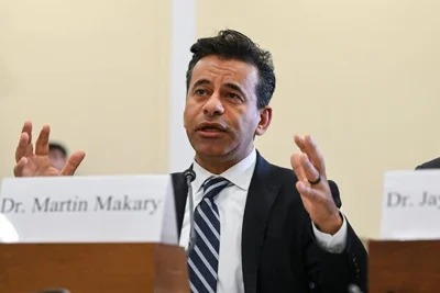 Dr. Martin A. Makary gestures as he speaks before a House subcommittee on the coronavirus. He sits at a table with other speakers with a name card propped up in front of him.