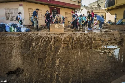 People wearing PPE try to sweep away mud as they desperately clean up the streets