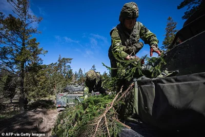 Soldiers of the P18 Gotland Regiment of the Swedish Army camouflage their armoured vehicles during a field exercise near Visby on the Swedish island of Gotland on May 17, 2022